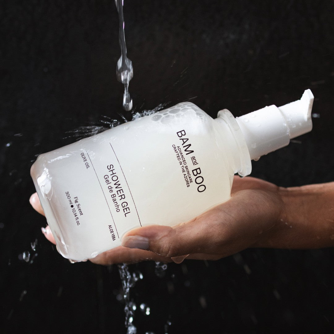 BAM and BOO shower gel bottle held by a hand with water droplets around it on a dark background. Natural hotel and home amenities.