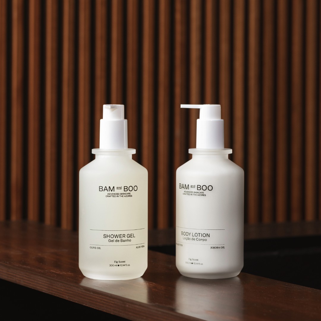 Two bottles of BAM & BOO shower gel and body lotion on a wooden surface with a wooden background. Natural portuguese amenities for hotels and spas.