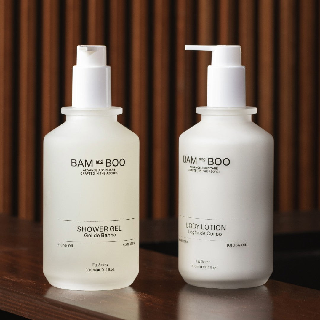 Two bottles of BAM BOO shower gel and body lotion on a wooden surface with a blurred brown background. Natural premium amenities for exclusive hotels.